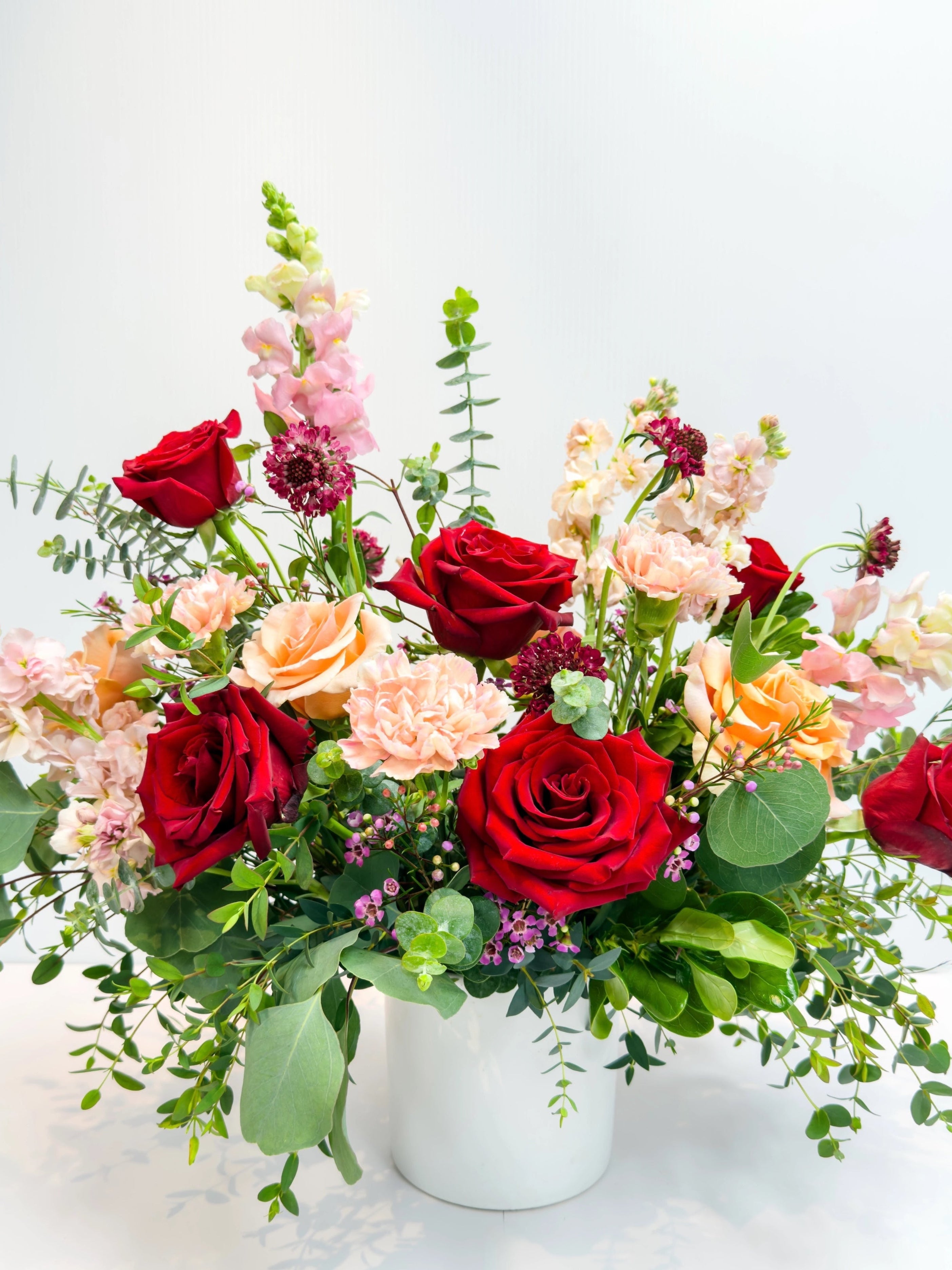 Bouquet of red, peach, and pink flowers in a white vase on a light background