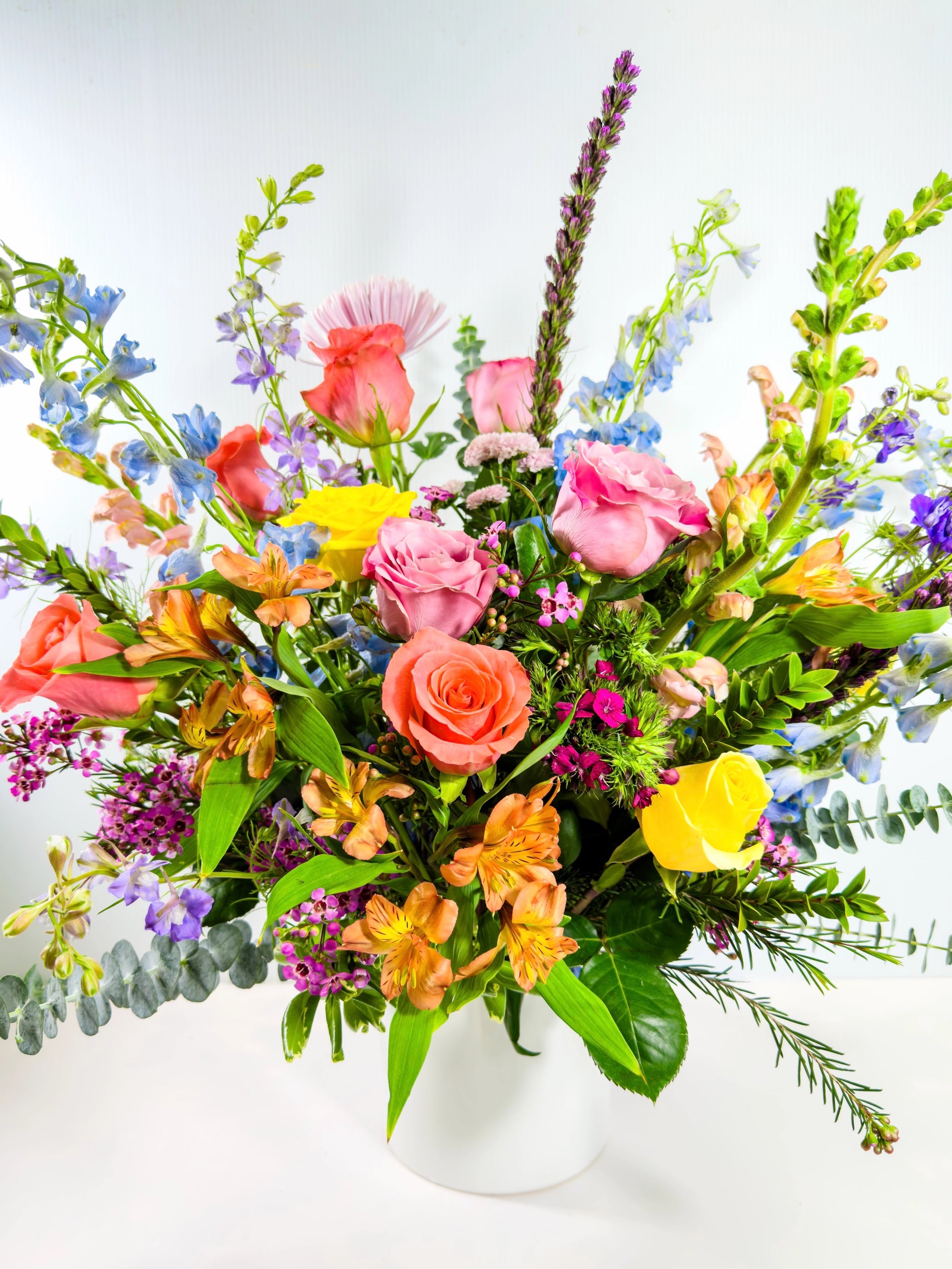Colorful flower bouquet with various types of flowers in a white vase on a light background